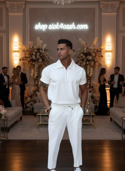 Person wearing a white polo shirt and pants against a gray wall.