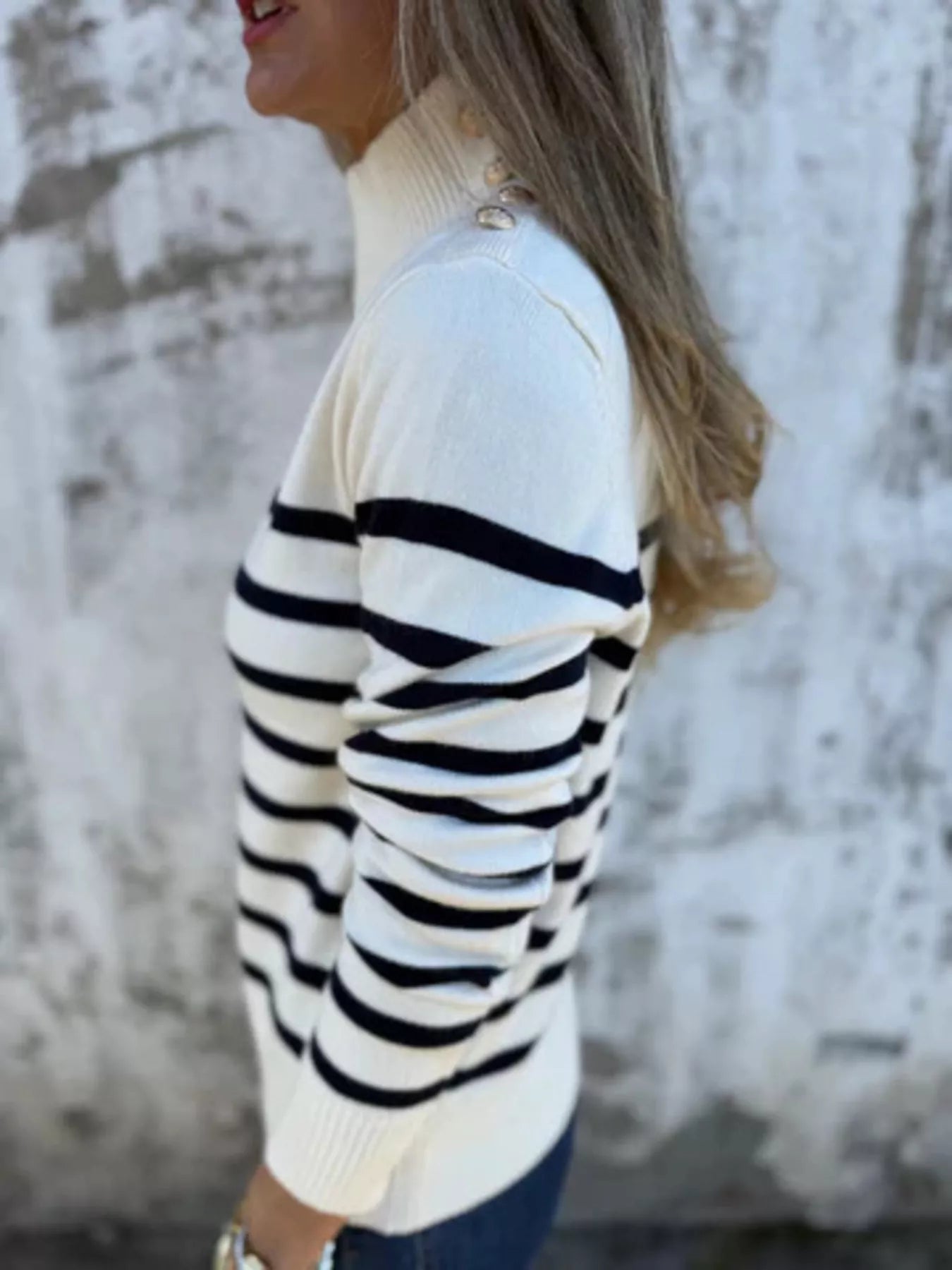 Person wearing a white sweater with black stripes against a blurred natural background