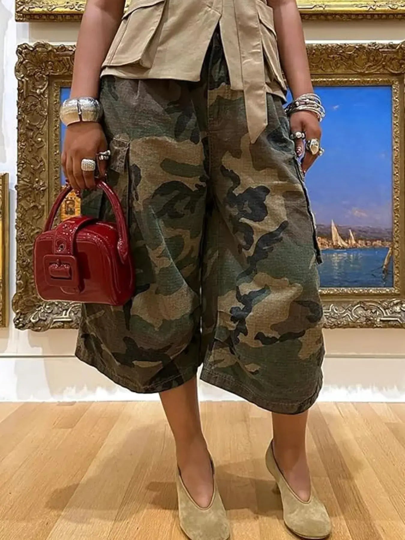 Camouflage Cargo Cropped Pants displayed with a red handbag and stylish accessories in an art gallery setting.