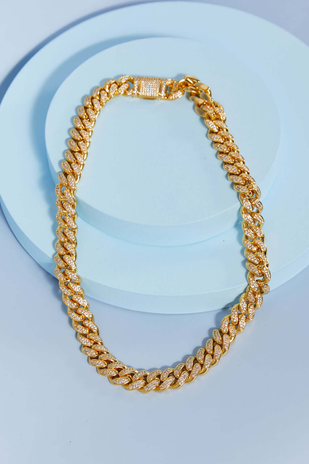 Brass Curb Chain Necklace displayed in a flat lay style on a light blue background, featuring cubic zirconia embellishments.