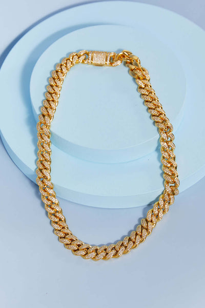 Brass Curb Chain Necklace displayed in a flat lay style on a light blue background, featuring cubic zirconia embellishments.