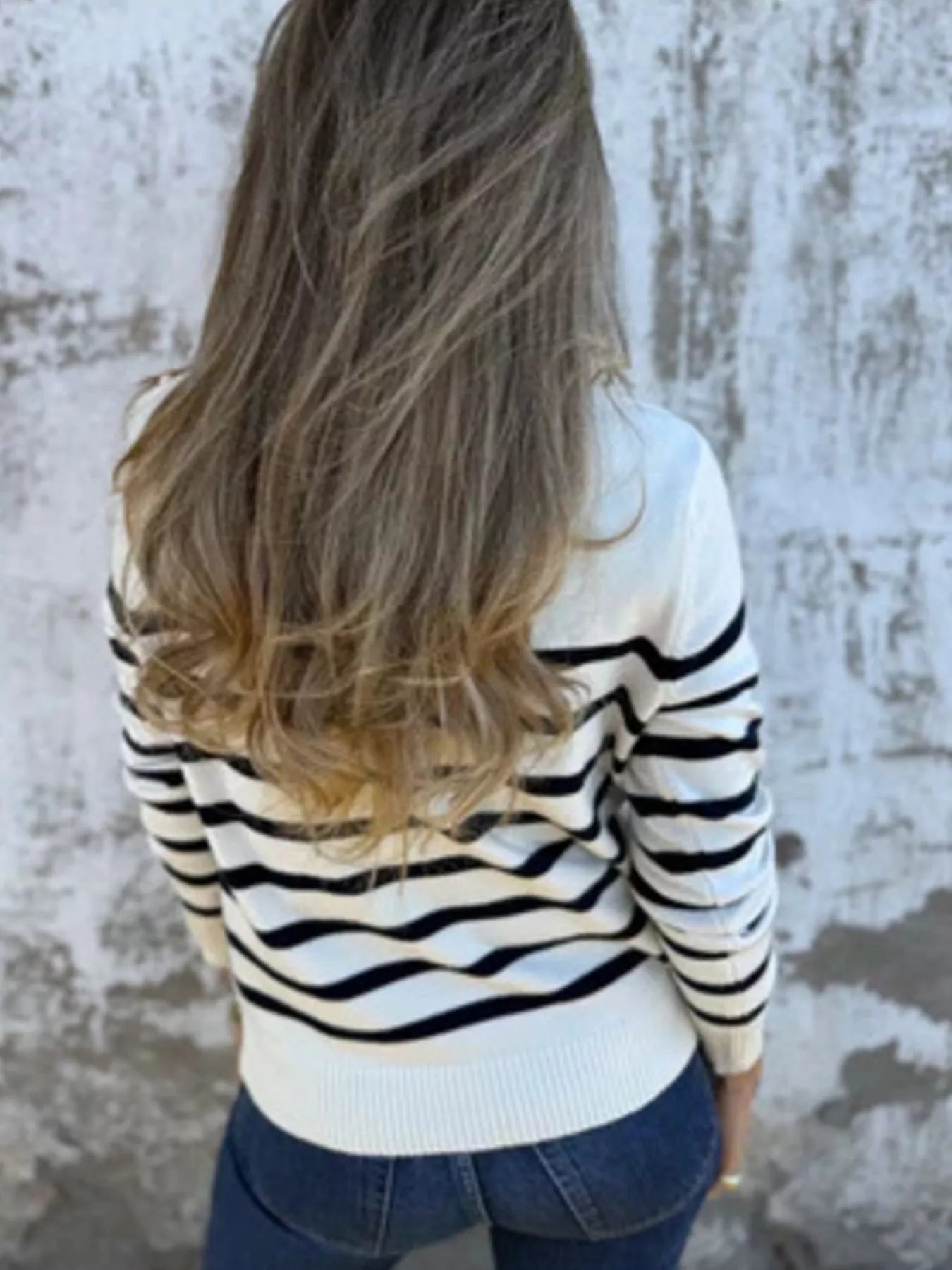 Person wearing a black and white striped sweater against a textured wall.