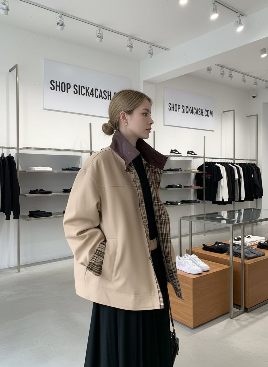 Person wearing a beige jacket with plaid accents against a gray wall.