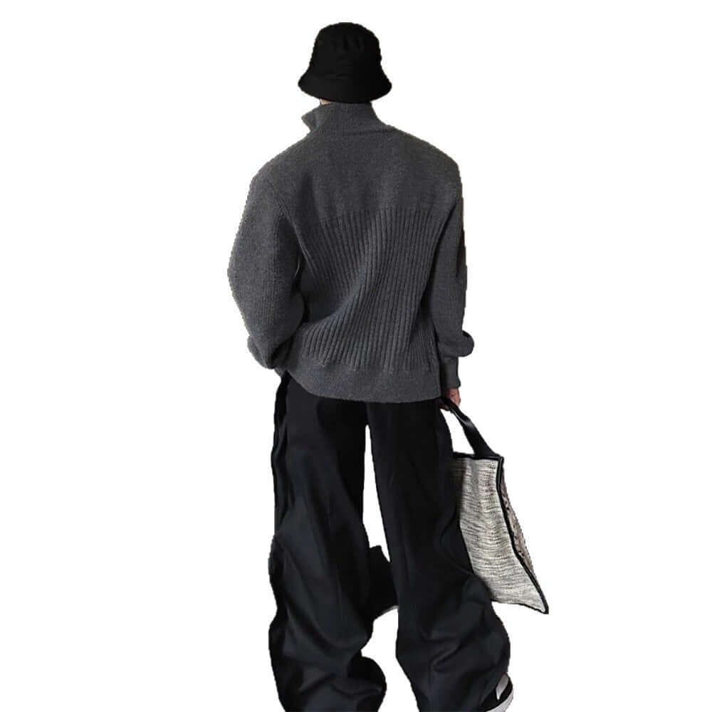 Person wearing a gray sweater with a patterned bag, standing on a balcony.