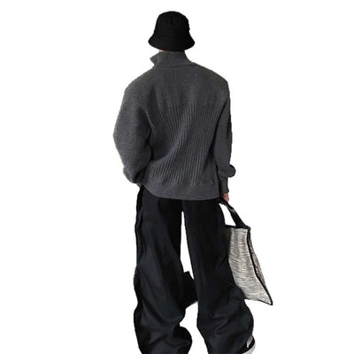 Person wearing a gray sweater with a patterned bag, standing on a balcony.