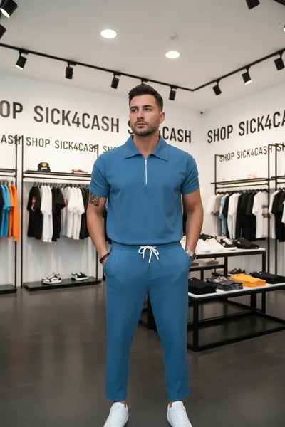 Person wearing a blue outfit with a matching polo shirt and pants against a light gray wall.