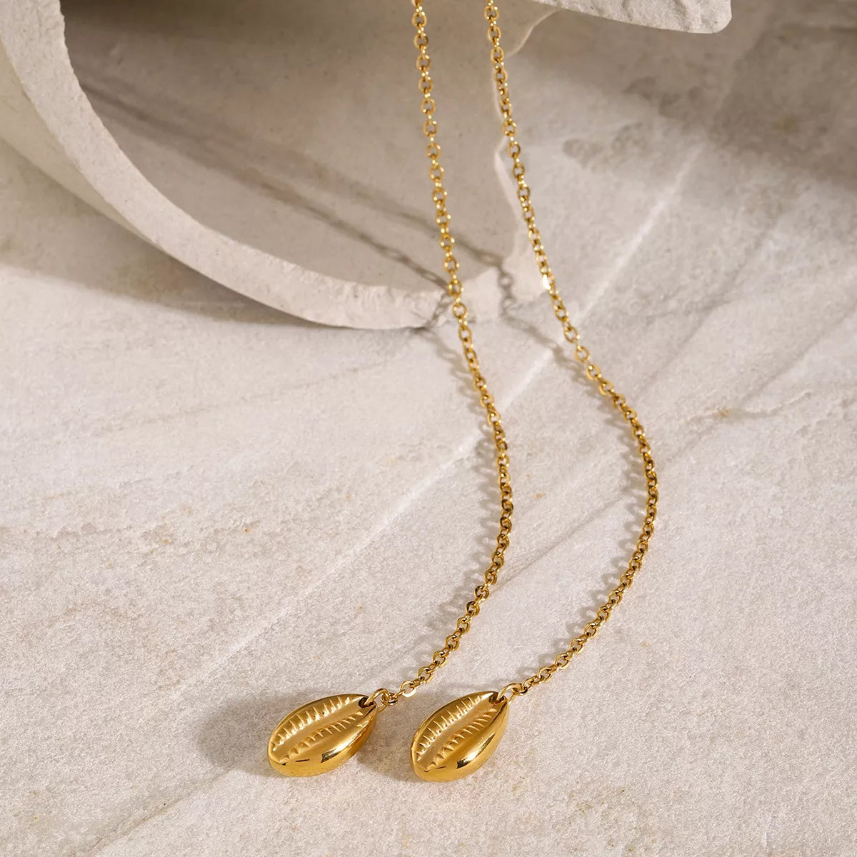 Gold necklace with leaf-shaped pendants on a textured beige surface