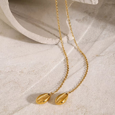 Gold necklace with leaf-shaped pendants on a textured beige surface