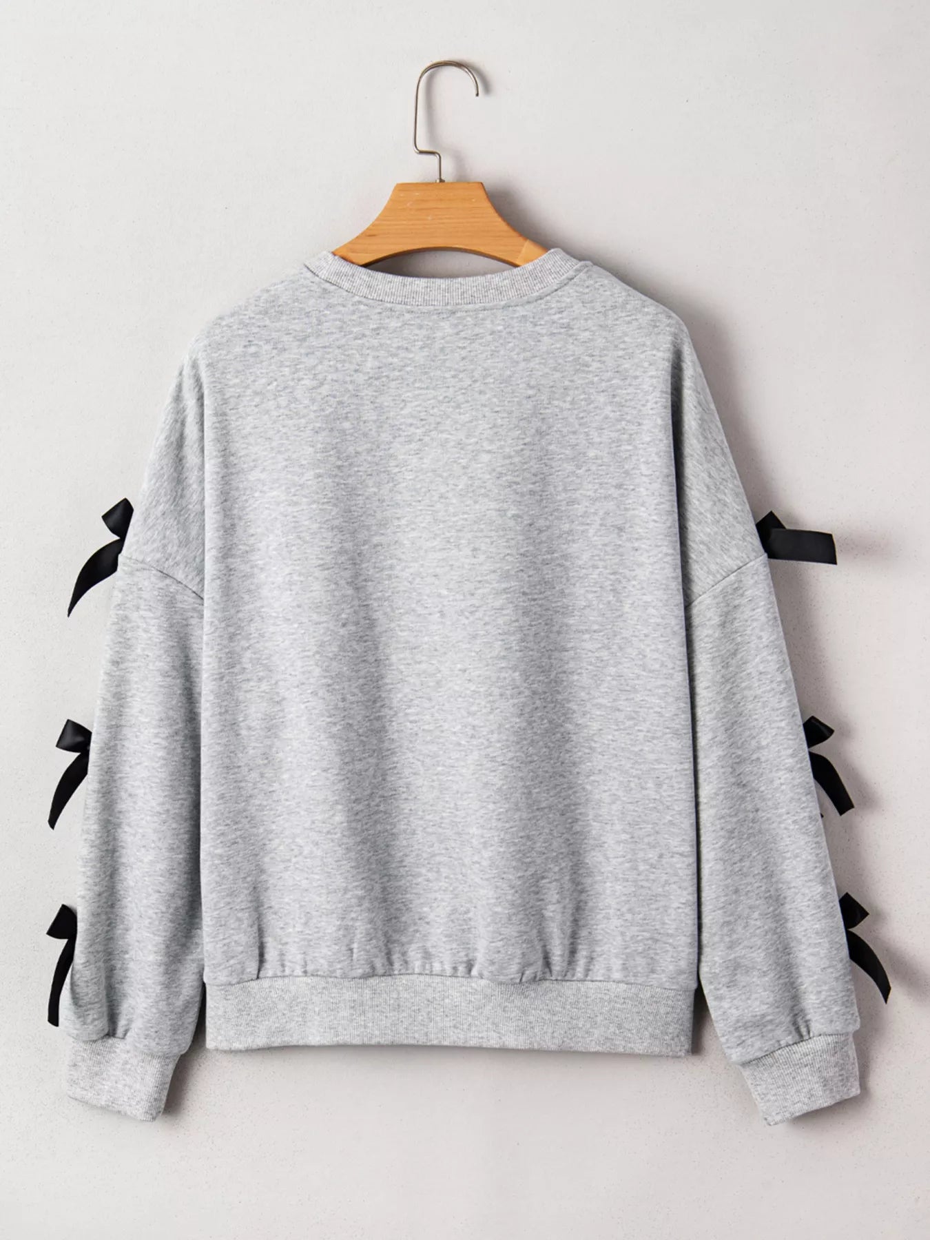 Gray sweatshirt with black ribbons on sleeves and back, hanging on a wooden hanger against a white background.
