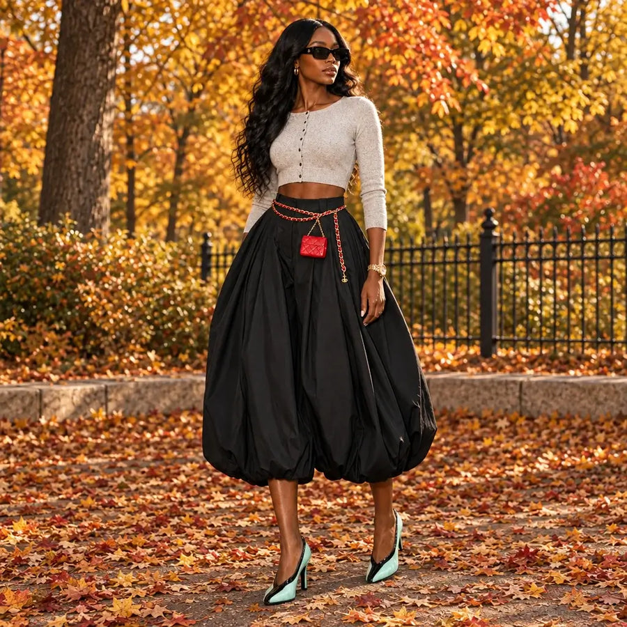 A person wearing a voluminous black high-waisted harem-style skirt with a gold chain belt and a small red crossbody bag, paired with mint green and black heels, standing on black diamond-plate steps in front of a cream paneled door.